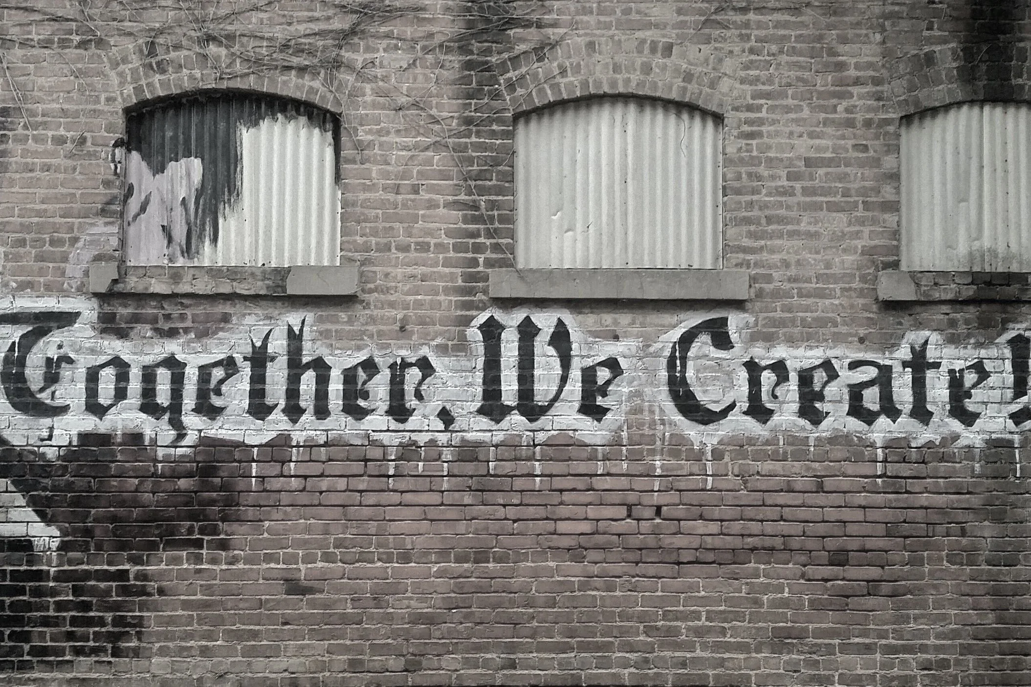 A brick wall with spray-painted graffiti that reads "Together, We Create" in black Gothic script.