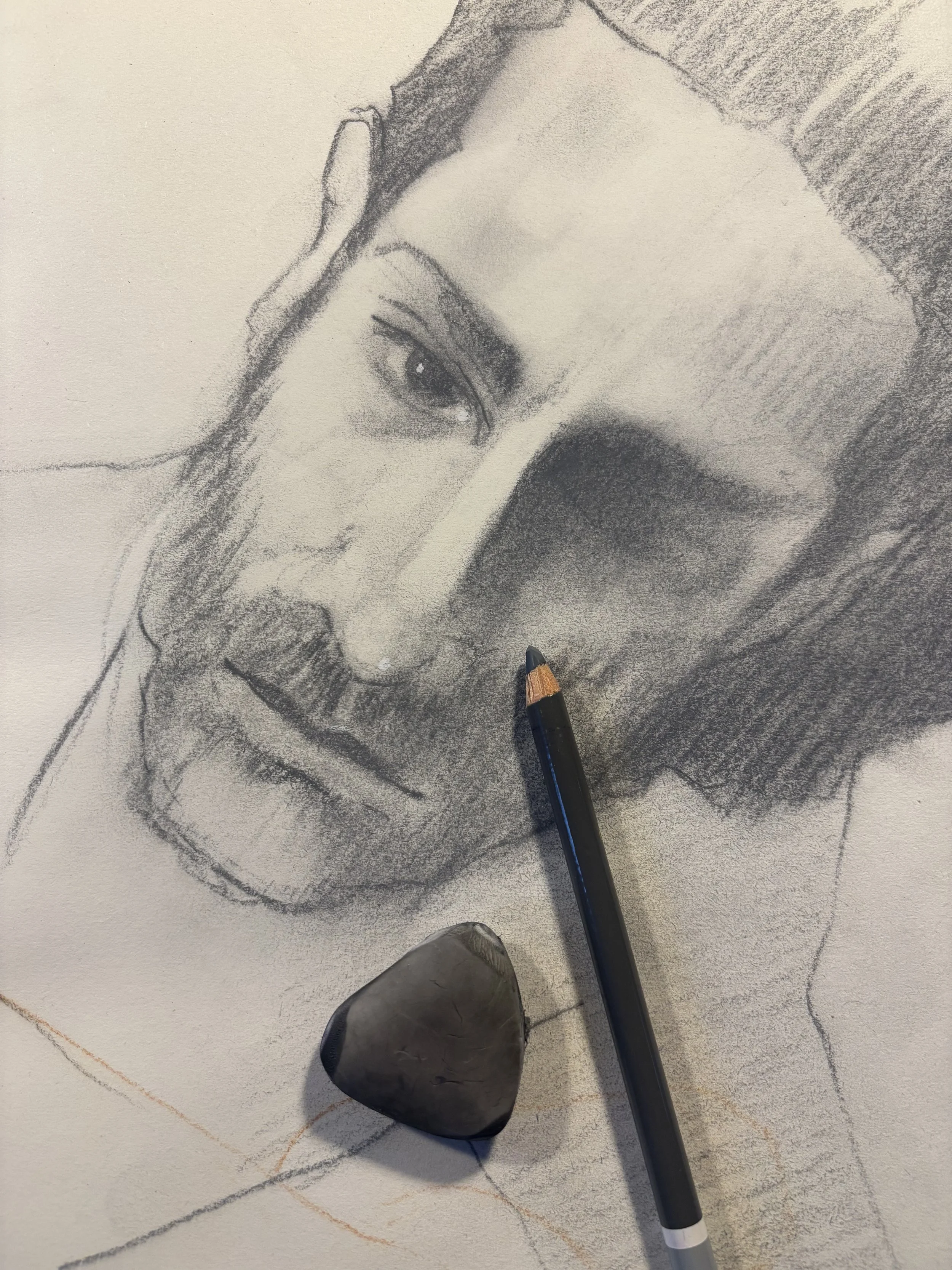 A detailed pencil drawing of a man's face with a focus on the eyes, nose, and lips, along with a pencil and a rubber placed on the drawing paper.