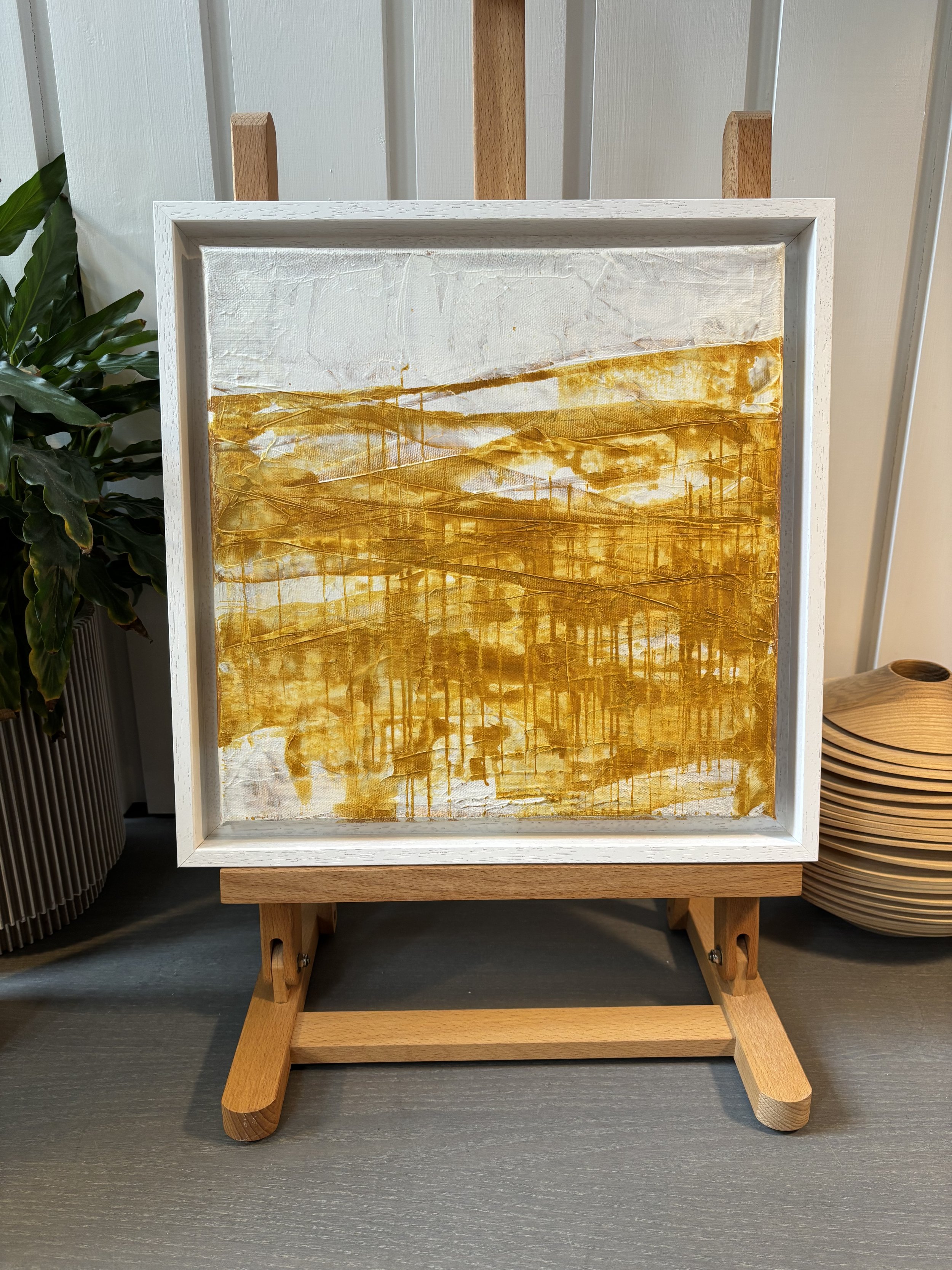 Abstract painting with yellow and white colors, featuring textured and layered brushstrokes, displayed on a small wooden easel.