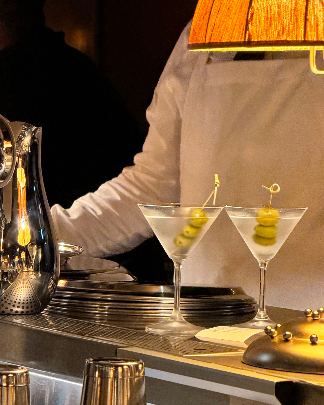 Two cocktail glasses garnished with green olives on toothpicks, placed on a bar counter near a shiny espresso machine.