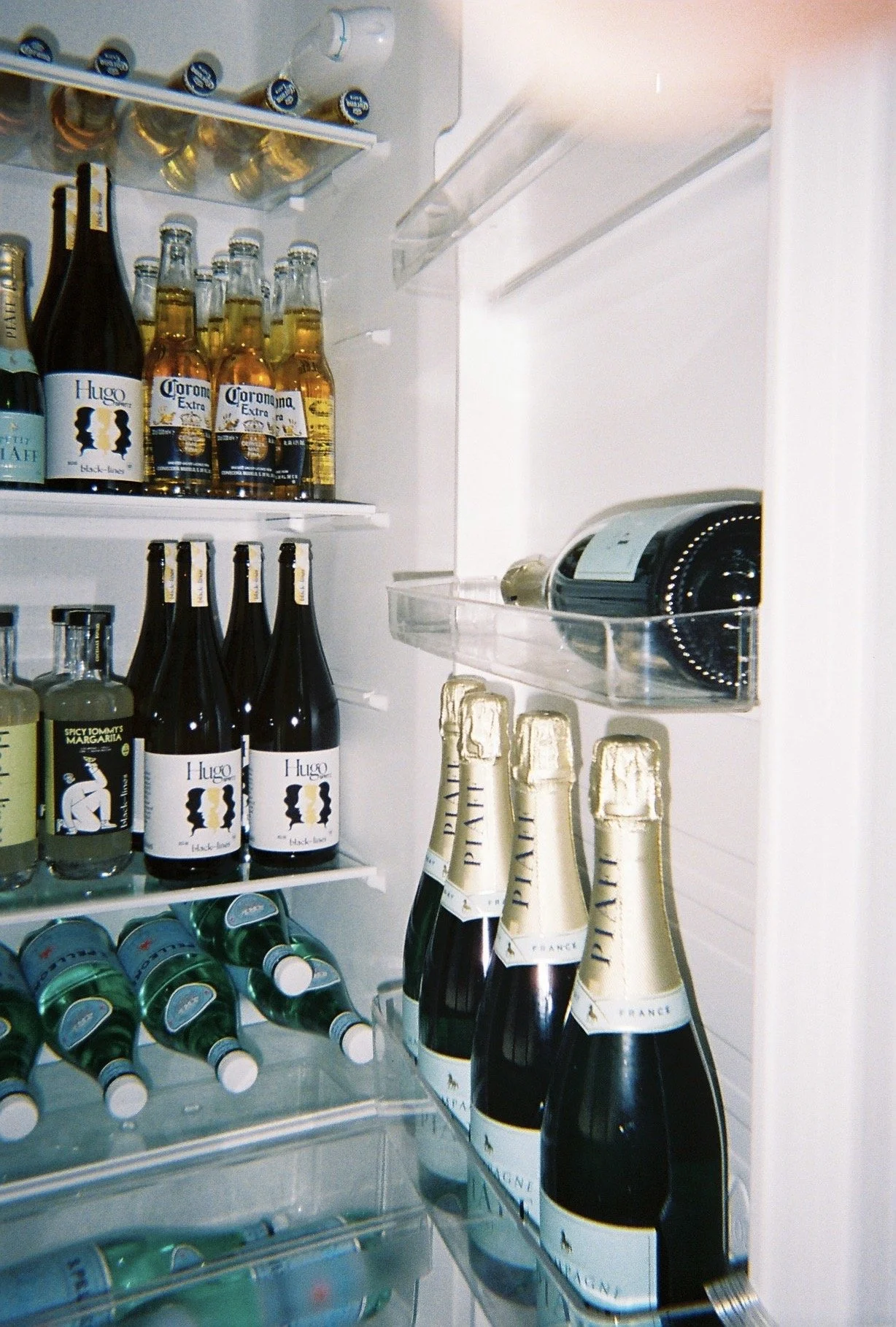 Inside a refrigerator with bottles of wine, beer, soda, and a wine cooler.