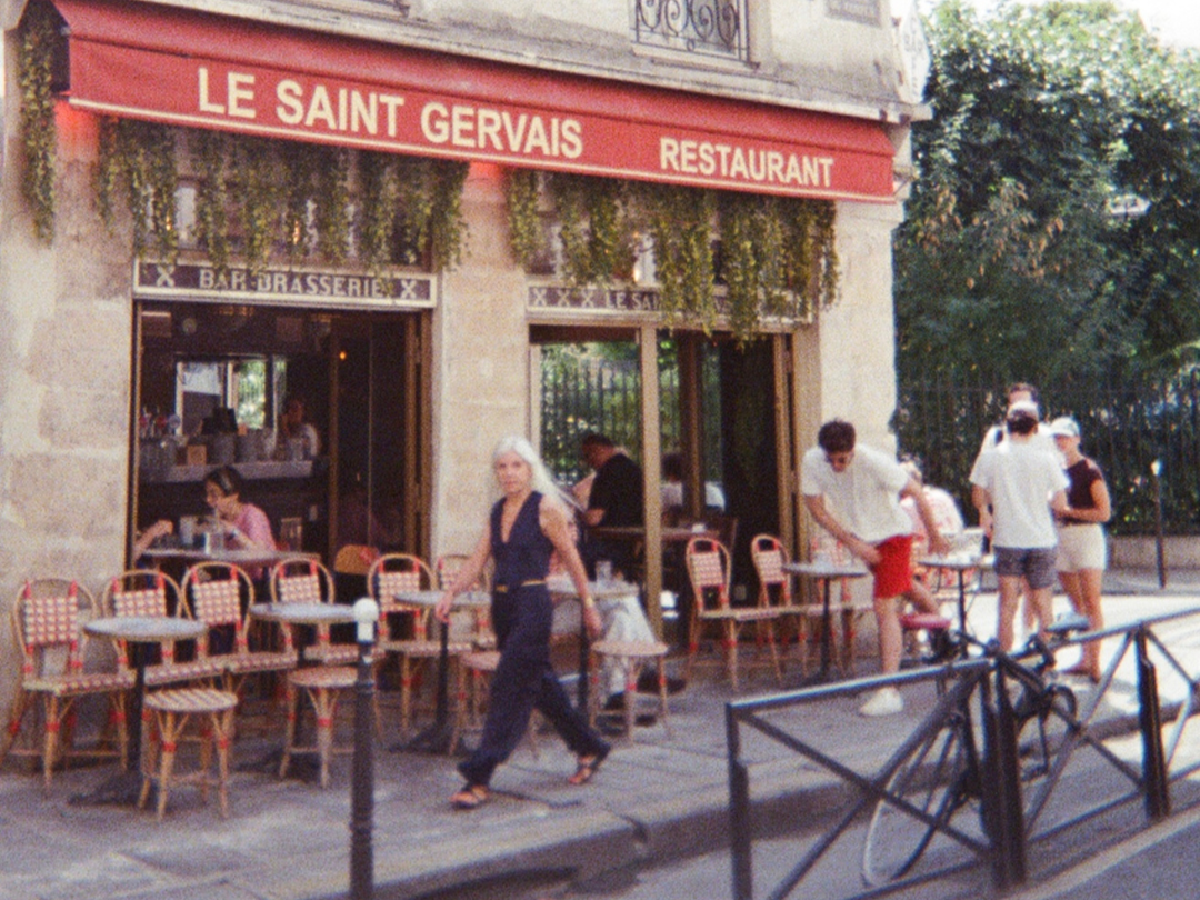 Outdoor view of the French restaurant 'Le Saint Gervais' with a red awning, patio seating, and people dining and walking outside.