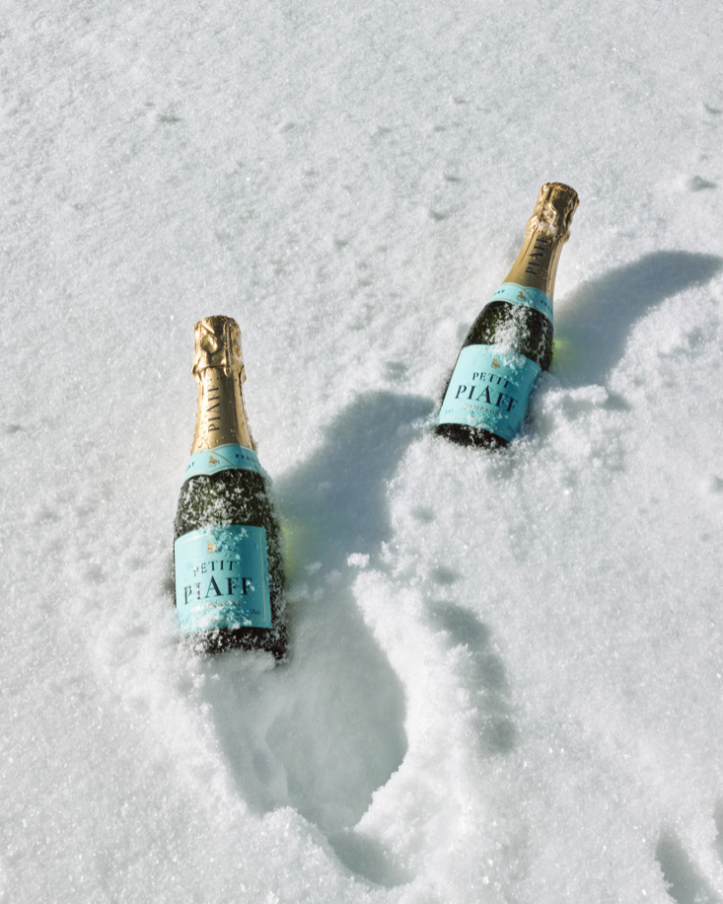 Two bottles of Petot Piaff sparkling wine partially buried in the snow with their labels visible.