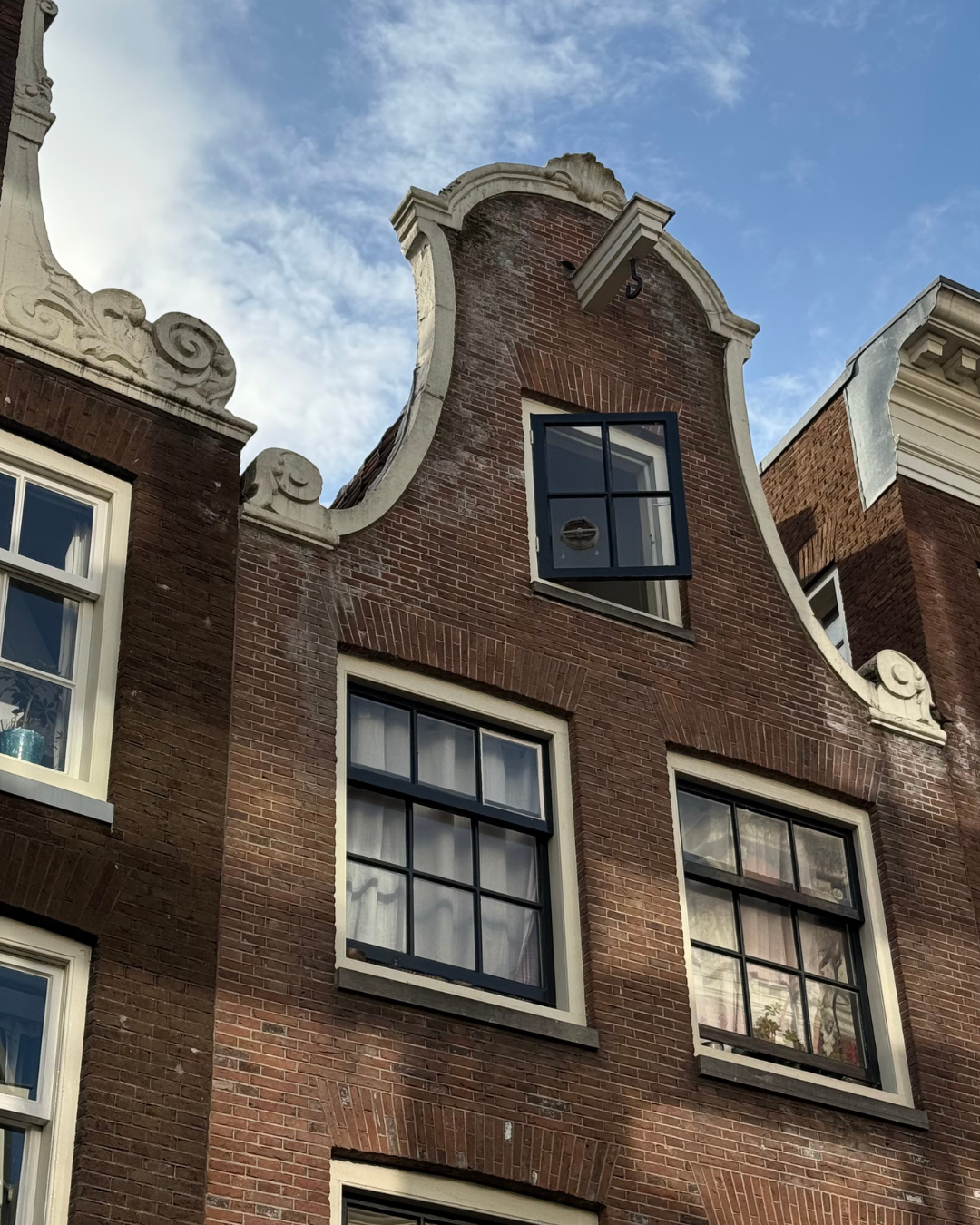 Close-up of a traditional Dutch-style brick building with ornate white stone decorative elements and large black-framed windows against a partly cloudy sky.