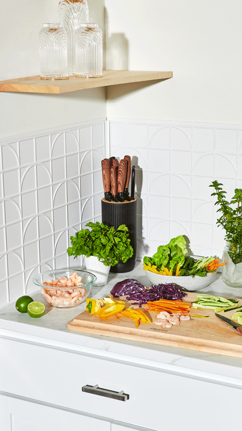 Kitchen countertop with rotating backgrounds. Countertop with fresh vegetables, lime, and shrimp, a knife block, and glass jars on a floating shelf