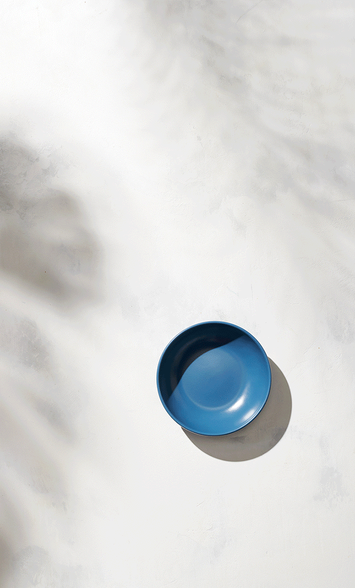 A blue circular bowl on a white surface with shadows cast around it.