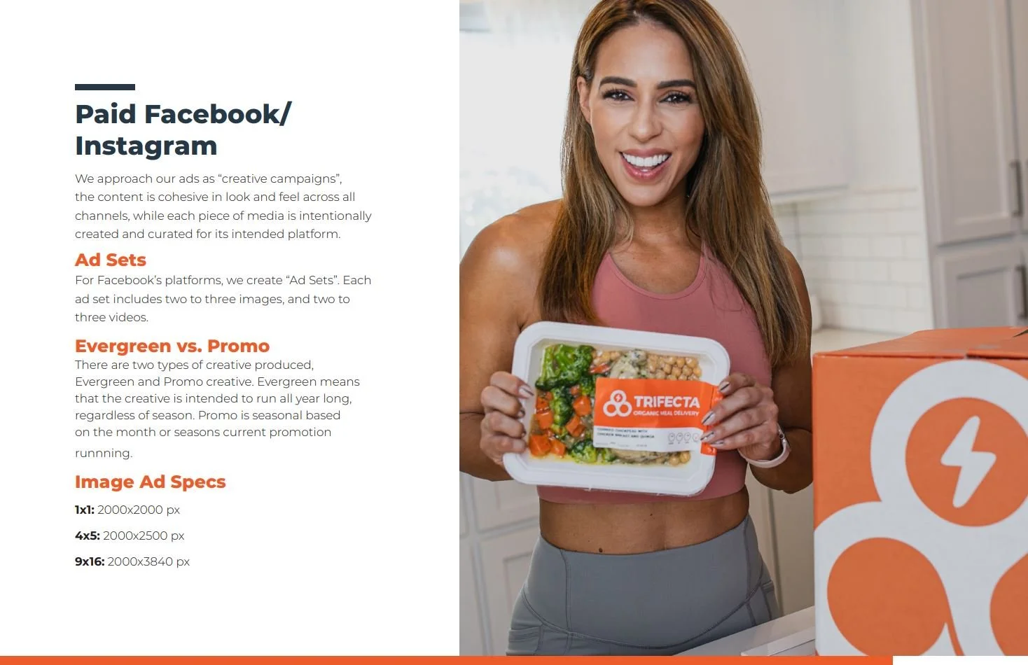 A woman smiling and holding a packaged meal from Trifecta organics while standing in a kitchen, with a large orange delivery box nearby.