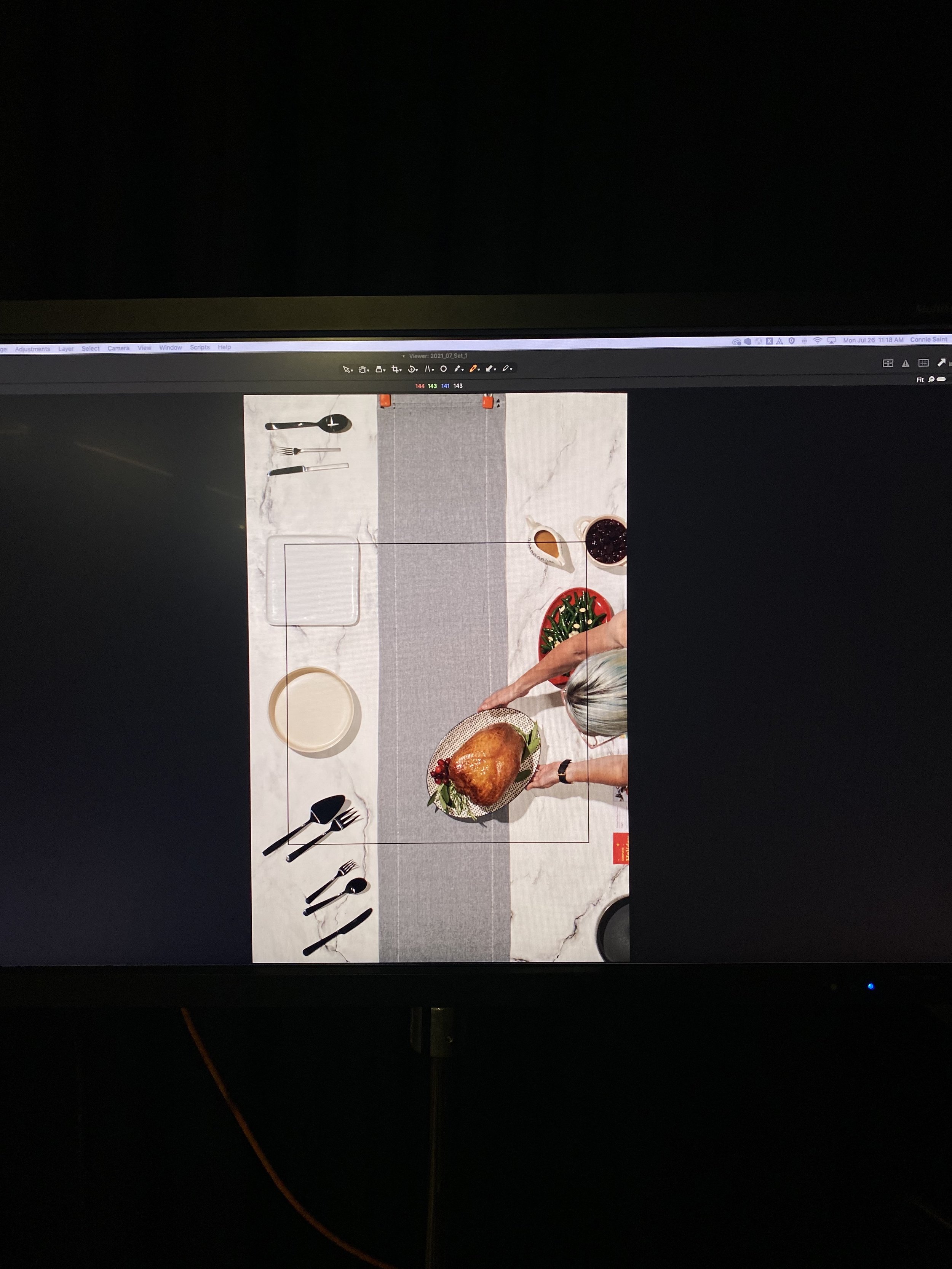A top-down view of a dining table setup with a person holding a platter with a roasted turkey, surrounded by plates, utensils, and bowls of sauces on a marble surface.
