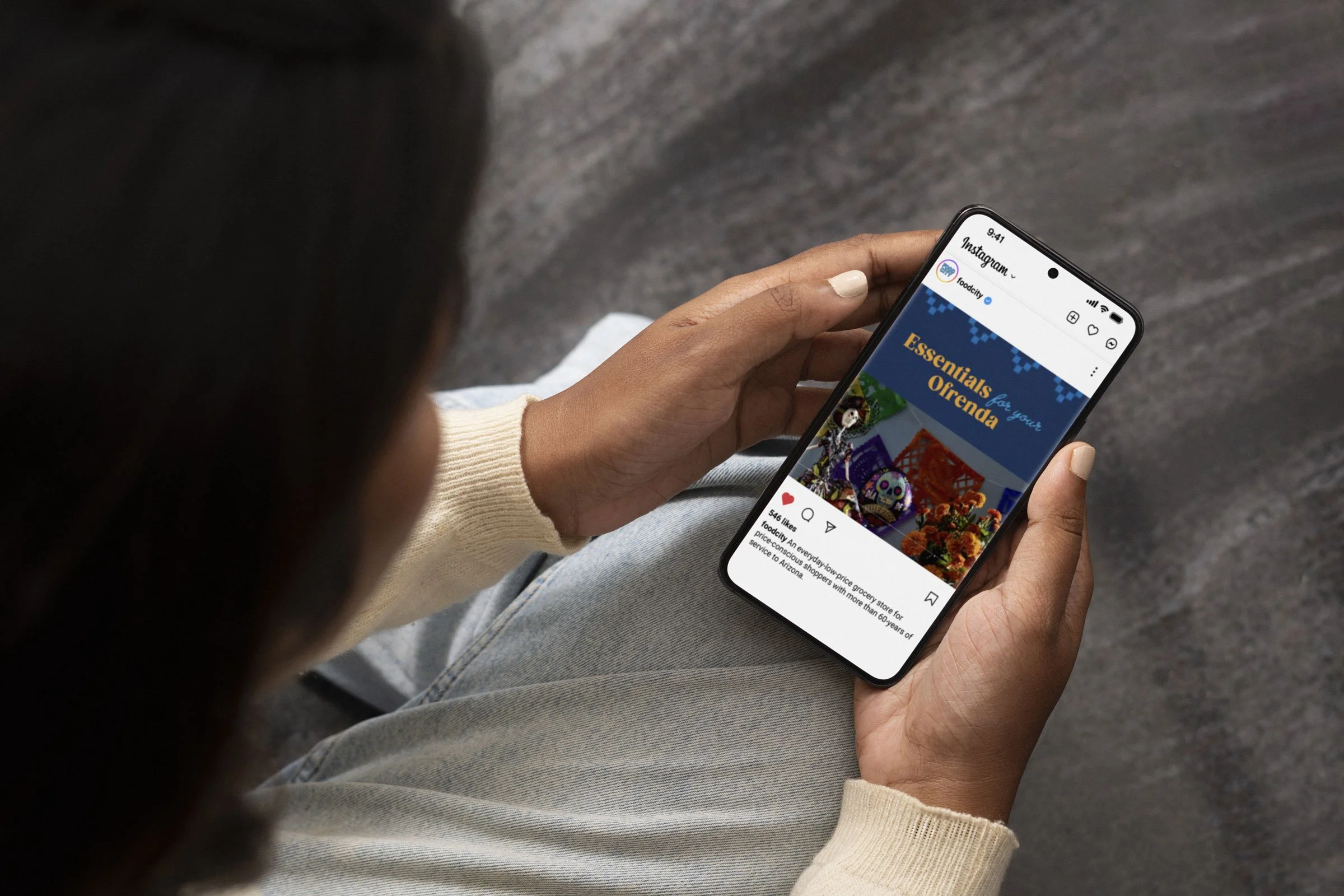 Person holding a smartphone displaying an Instagram post about food and grocery essentials, with colorful decorations in the background.
