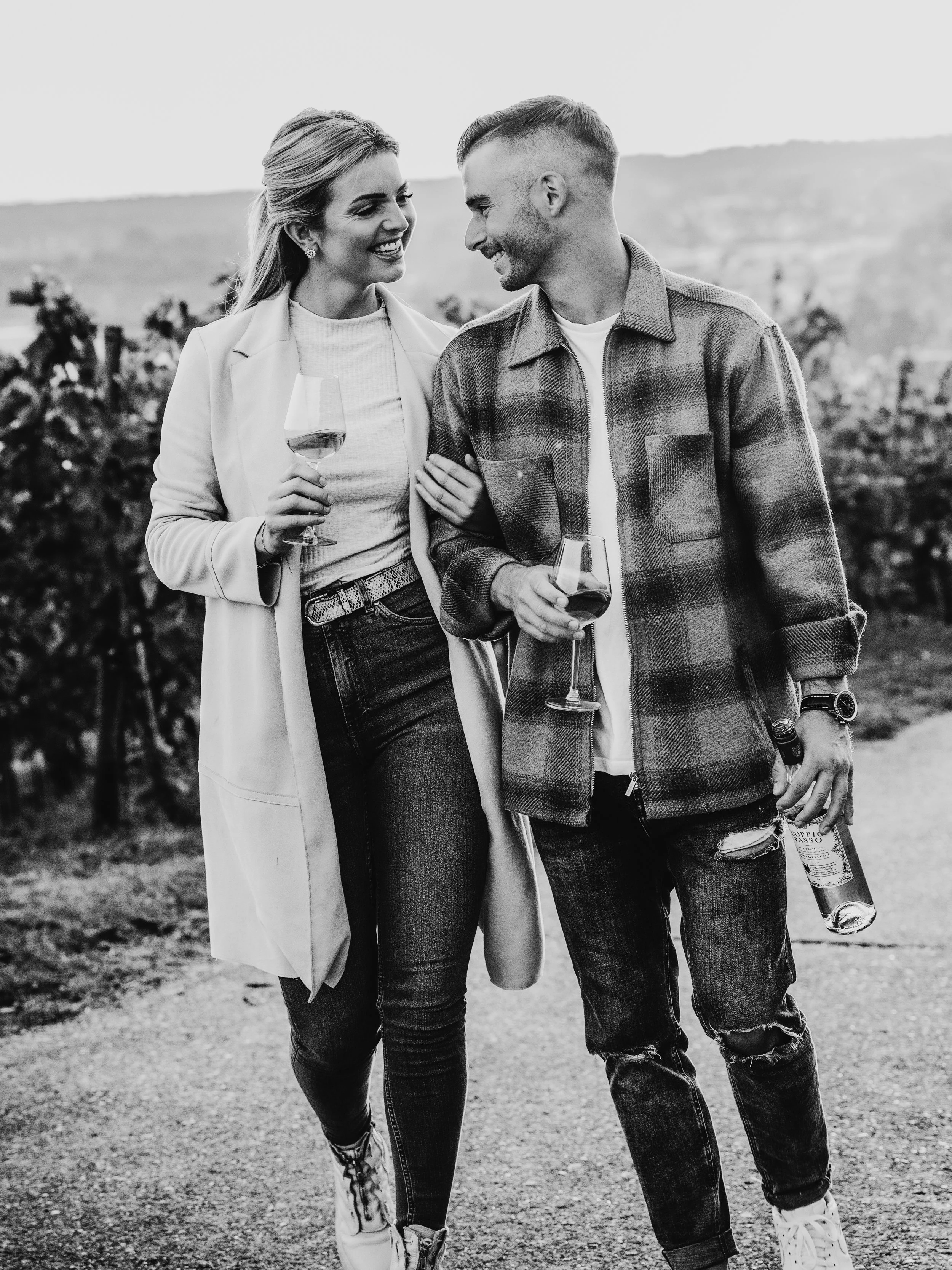 Ein lachendes Paar beim Weingenuss in einem Weinberg, schwarz-weiß aufgenommen.