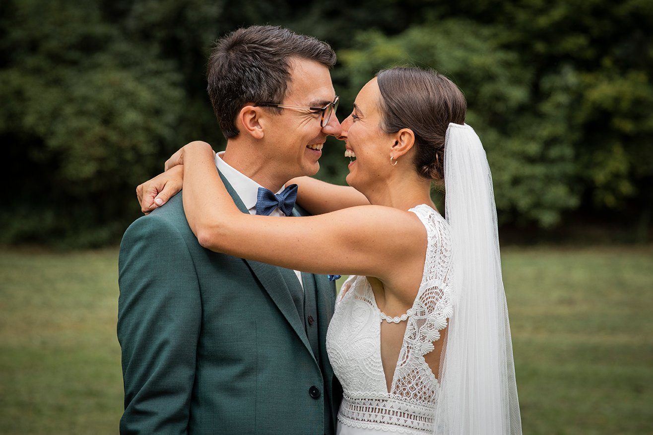 Ein Brautpaar, das sich lachend gegen einen grünen Hintergrund umarmt.