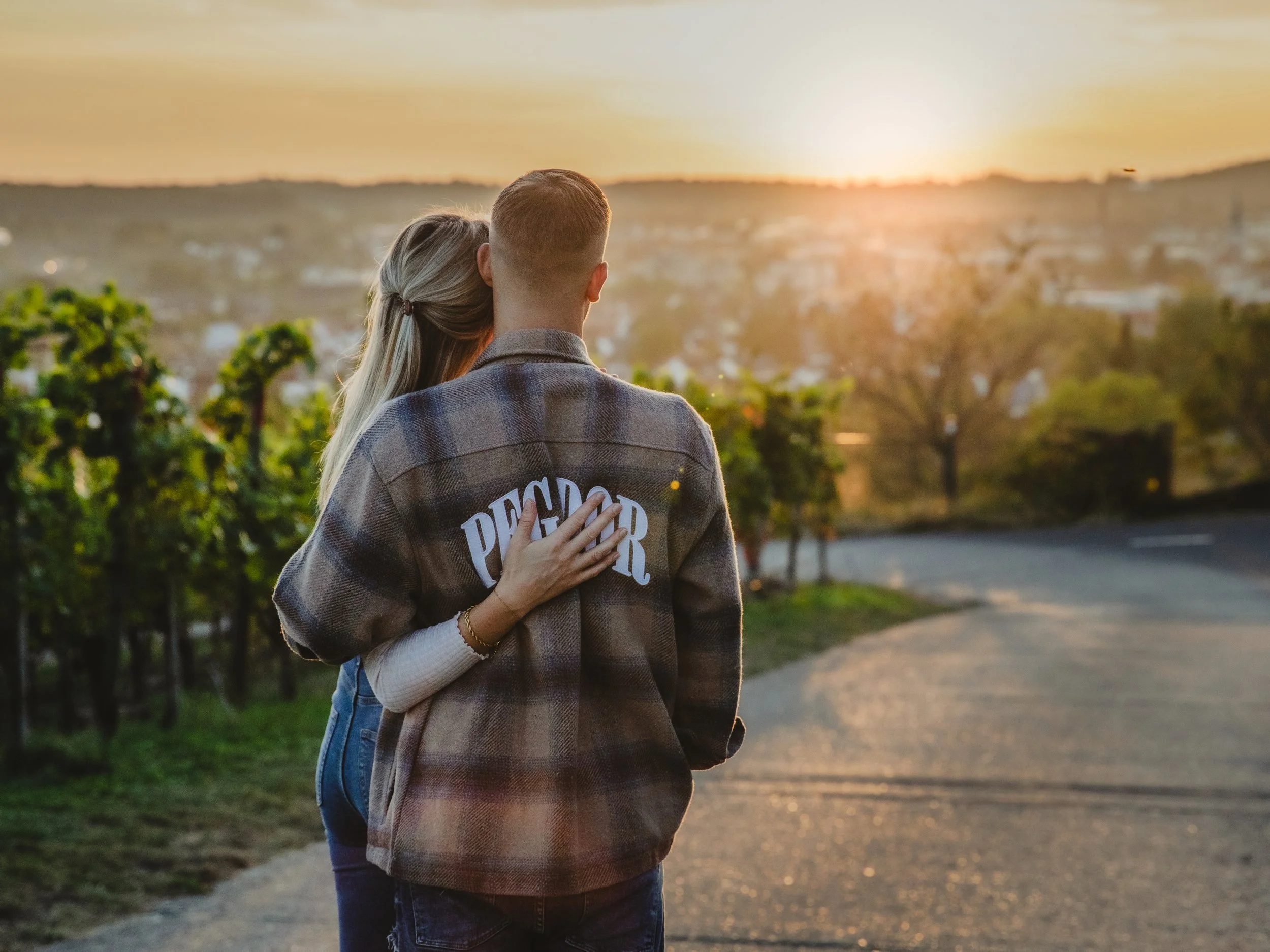 Ein Paar steht an einer Straße während eines Sonnenuntergangs, umarmt sich und blickt in die Ferne.