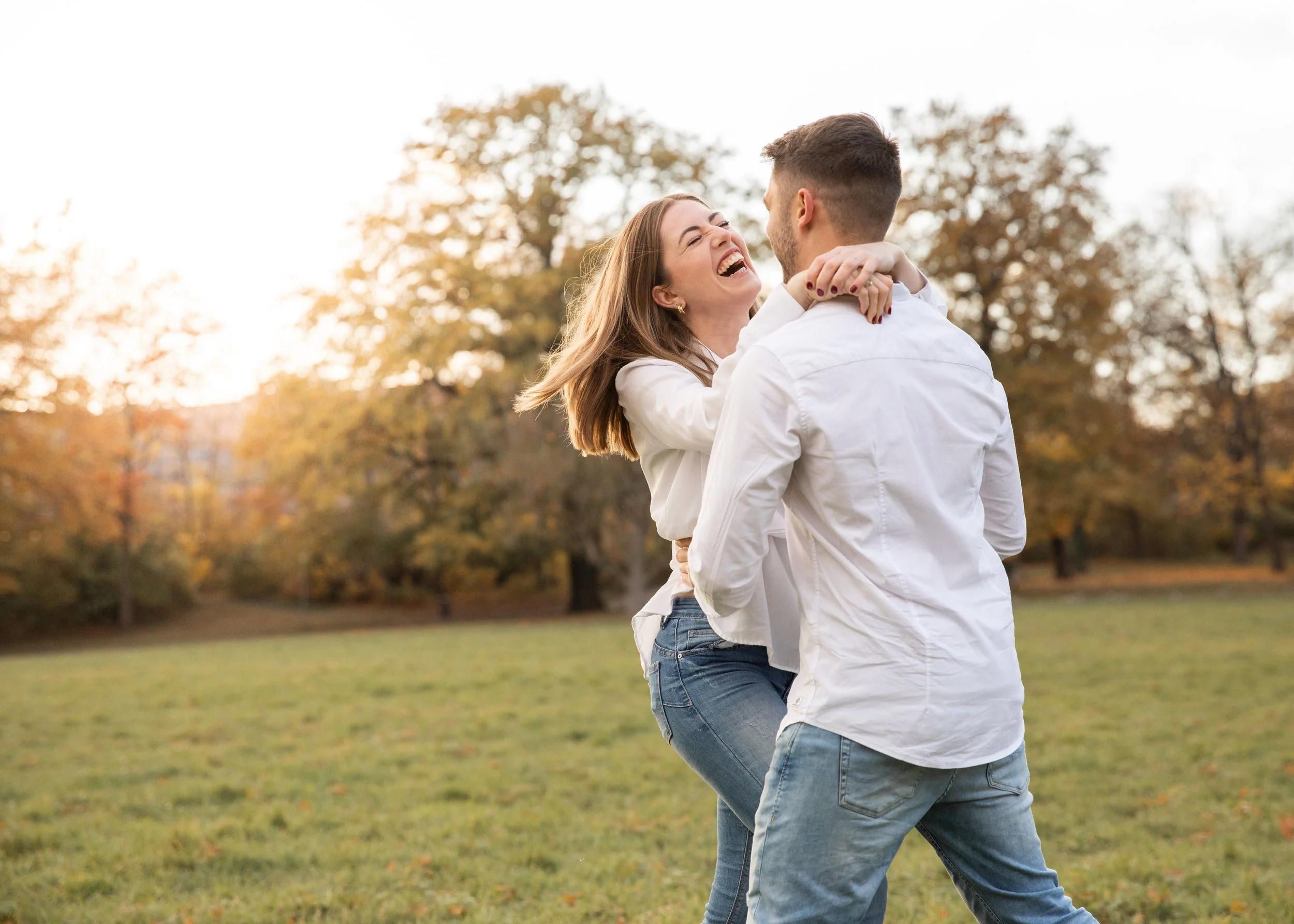 Ein lachendes Paar tanzt im Park im Herbst, umgeben von bunten Bäumen.