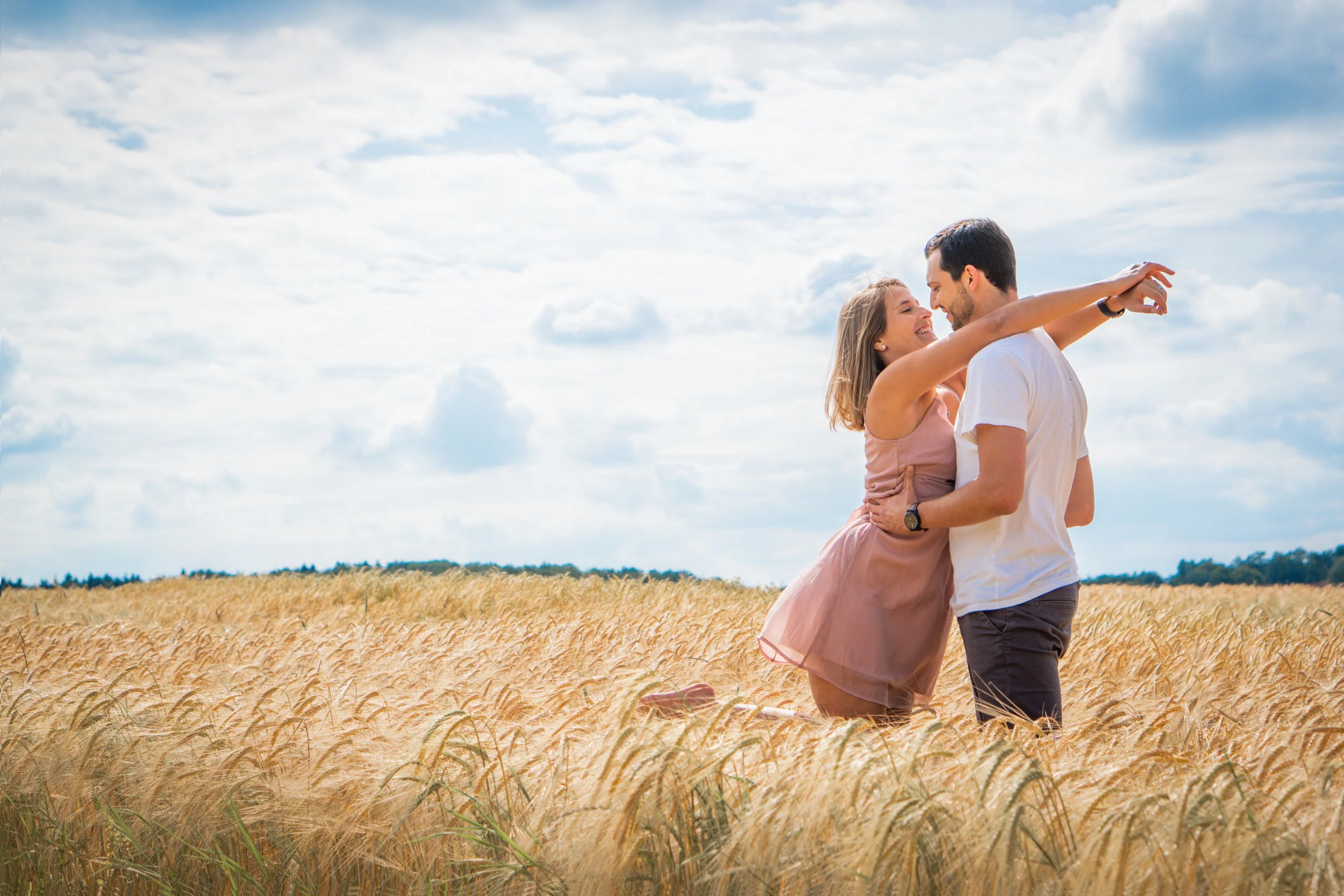 Ein glückliches Paar umarmt sich in einem Weizenfeld unter einem bewölkten Himmel.