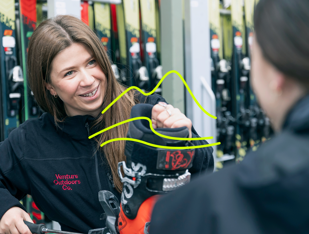 Venture Outdoors Co. staff member helping a student fit ski boots in the gear hire area.