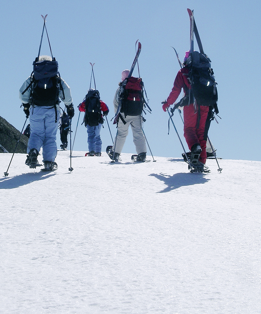 Students hiking with skis across a snowy ridge during a backcountry program.