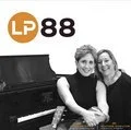 Two women sitting together at a piano, smiling for the camera.