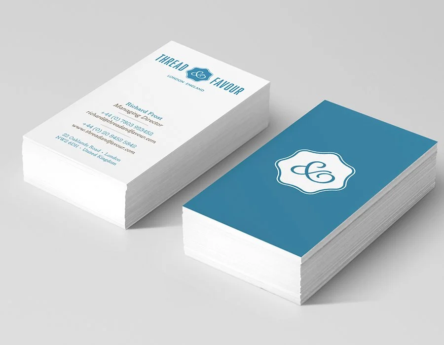 Two stacks of business cards, one with a blue background and a white logo, and the other white with blue text and contact information for Thread Favour, a London-based company, including a logo, company name, tagline, contact person, and address.