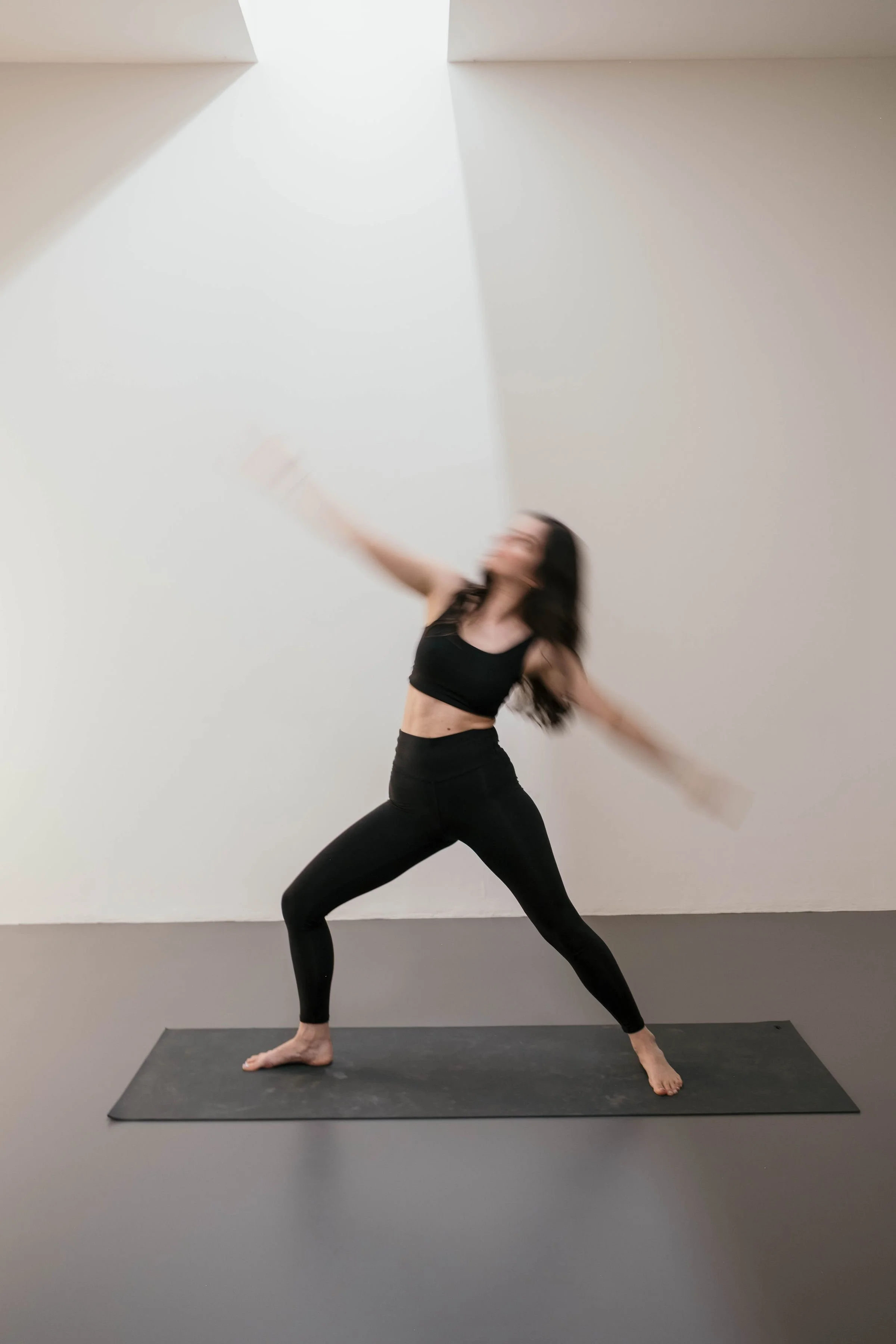 Frau beim Yoga in einer minimalistischen, hellen Raum steht in einer seitlichen Warrior-Position auf einer Matte.