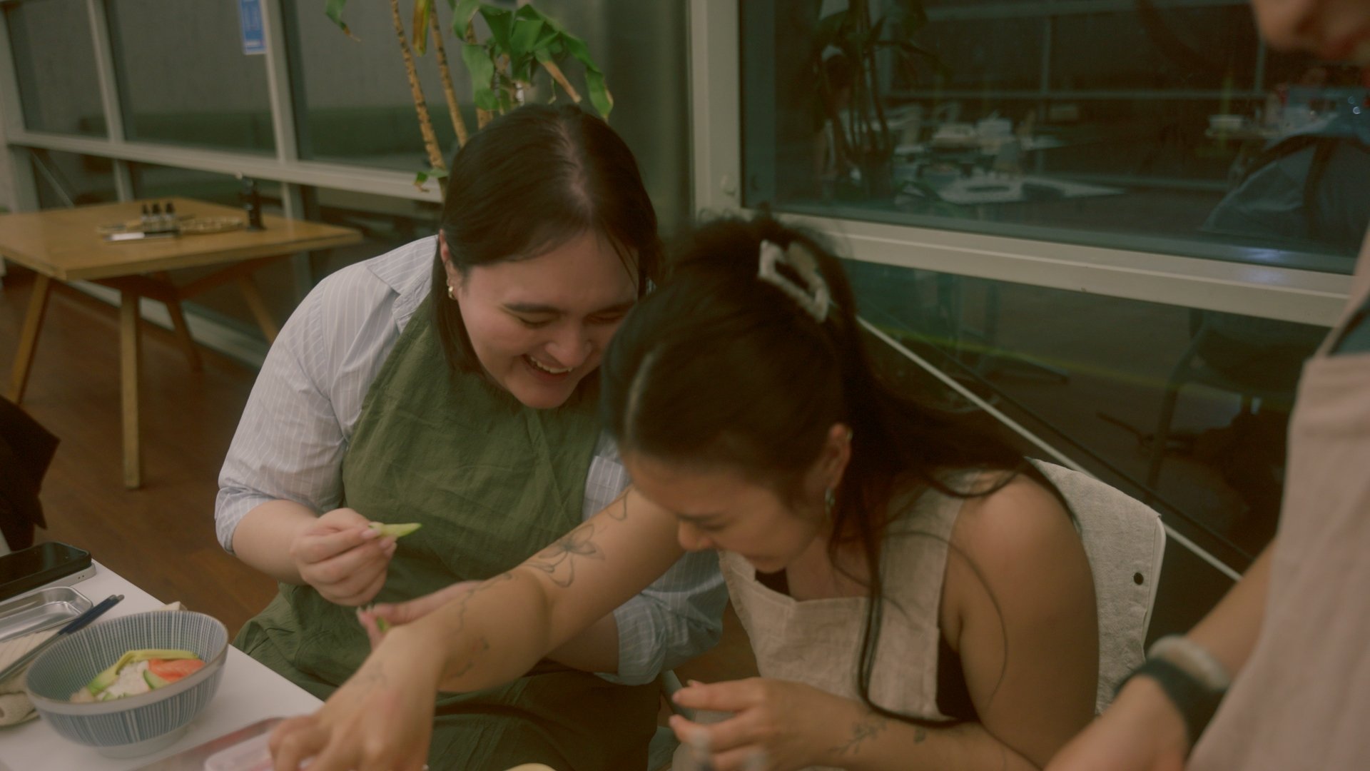 Two women smiling and laughing while getting their tattoo done in a tattoo studio.