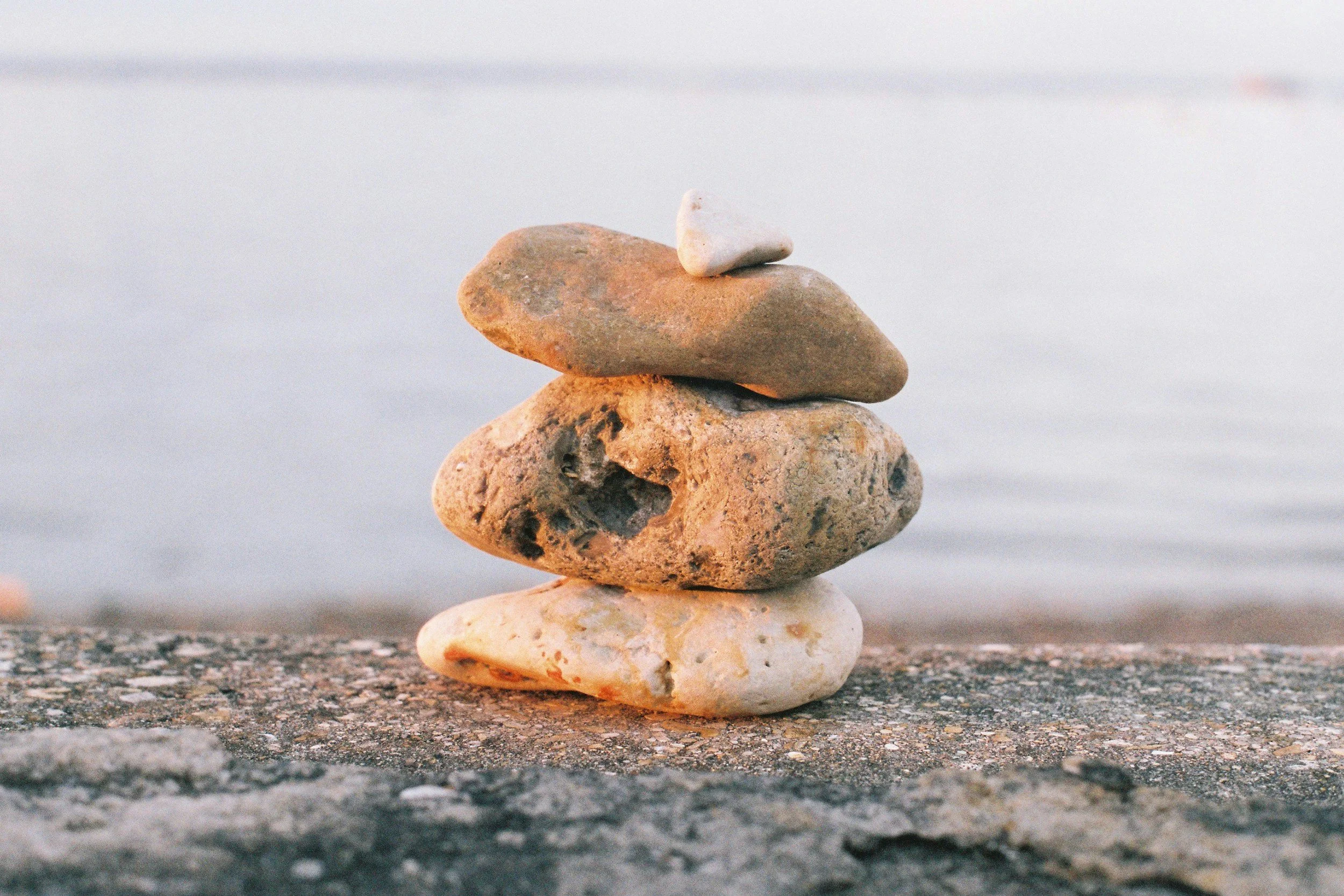 Stack of balanced stones on a seafront symbolising the personalised, empowering, and accountable principles of JUST Alex