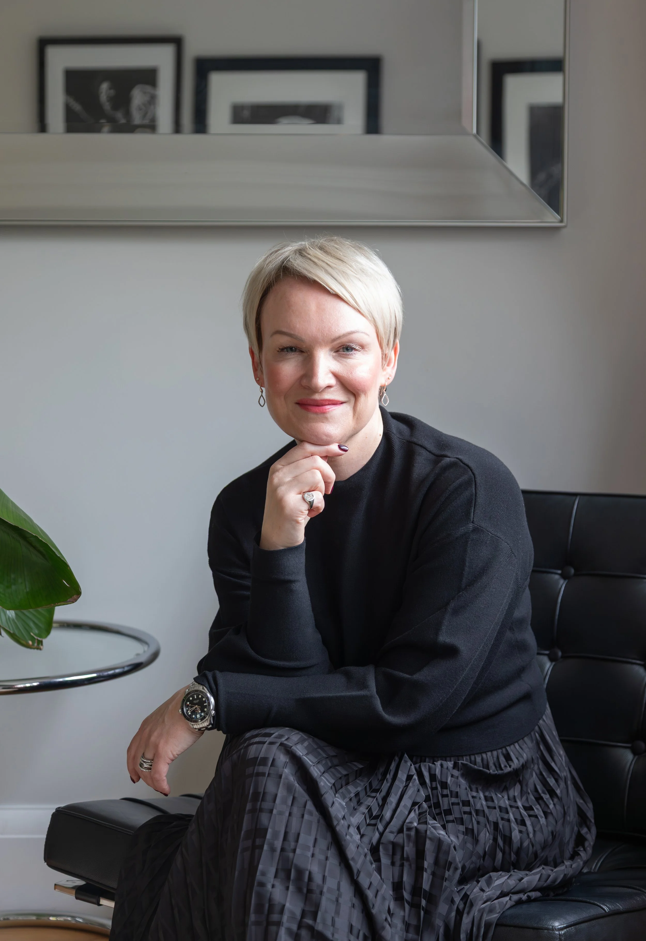 Alex Akrimi seated in a bright, relaxed setting, smiling confidently in a natural light portrait.