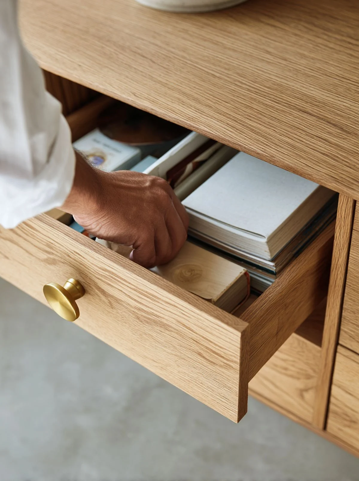 Person opening a wooden drawer containing notebooks, books, and small boxes.