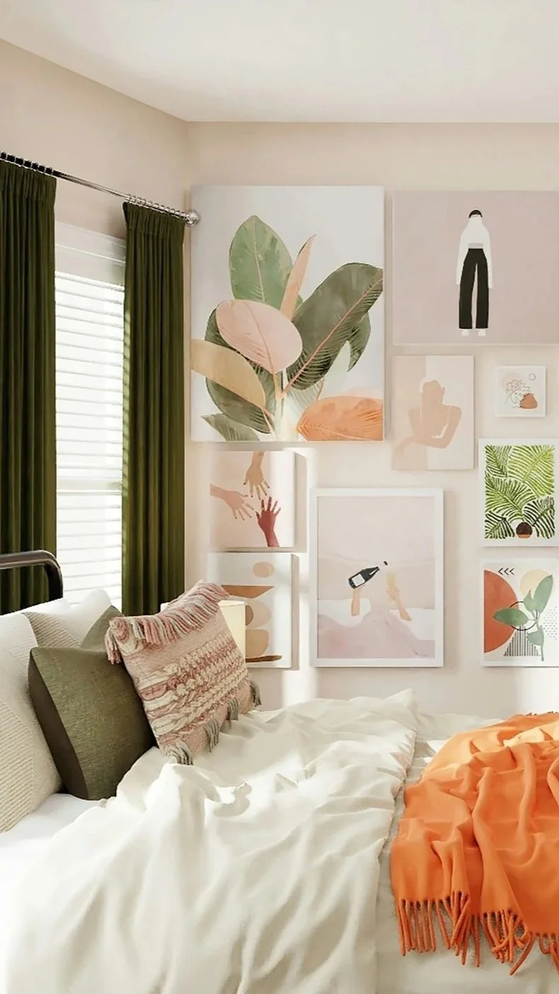 A bedroom with a white bed, multiple pillows, and an orange blanket. The wall above features a gallery of art prints including a large botanical print, abstract human figures, and leafy designs. There are green curtains covering a window with blinds.
