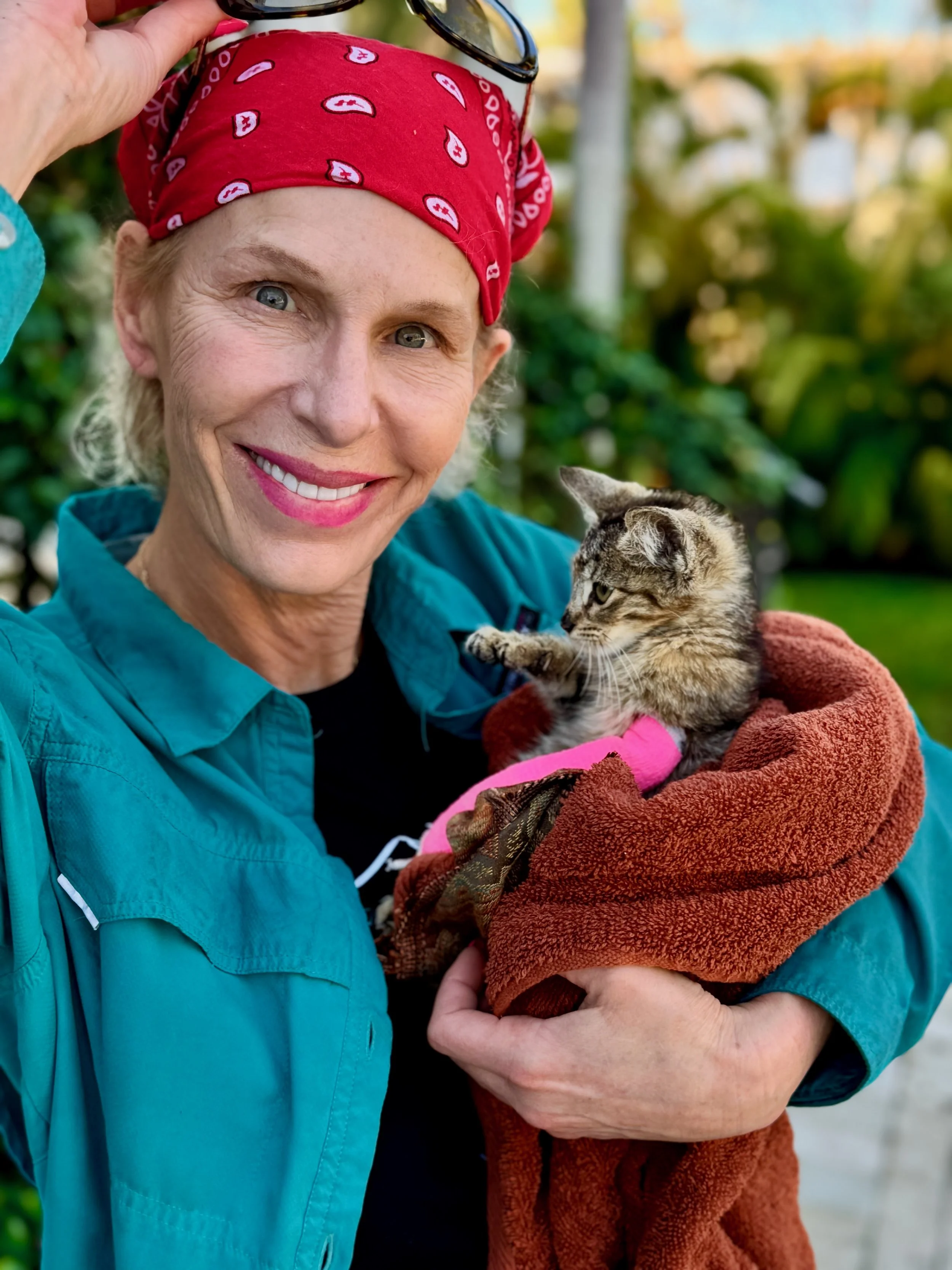 Danna Stillman smiling while holding an injured small tabby kitten wrapped in a red and brown blanket.