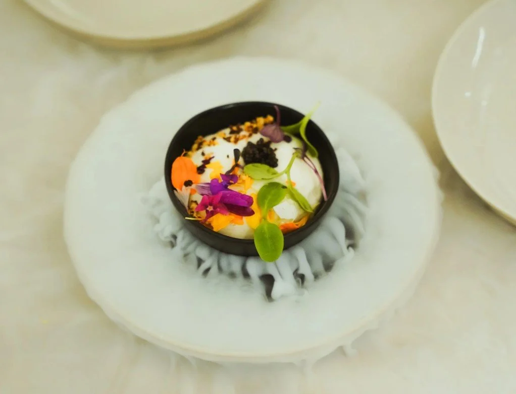 Plaque de fromage blanc ou de yaourt avec des fleurs comestibles et des micro-pousses, décorée dans un petit bol noir.