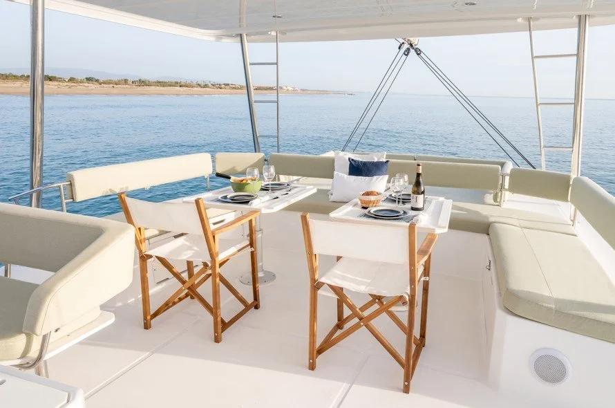 Table de dîner avec assiettes, verres, bouteilles, et chaises, sur un bateau avec vue sur l'océan