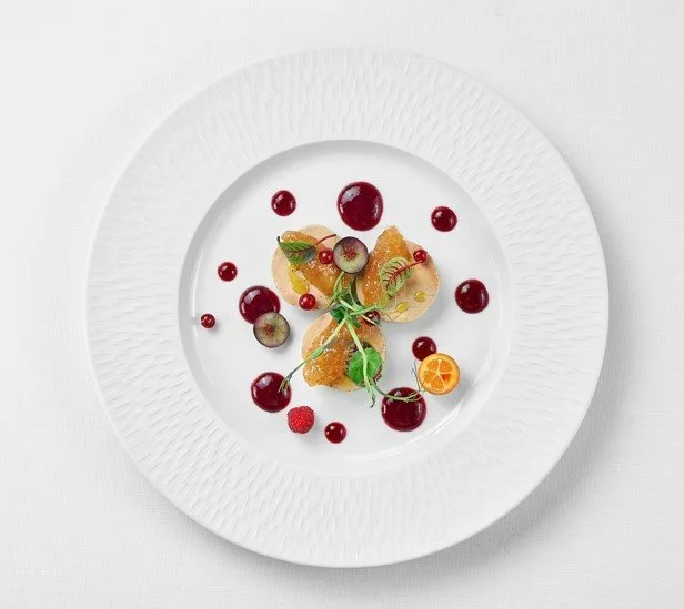 Assiette avec une présentation de dessert à base de fruits rouges, agrumes, et feuilles de menthe