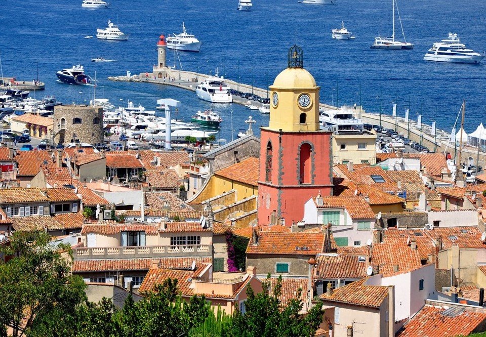 Vieux village méditerranéen avec une église à clocher et un port avec des yachts.