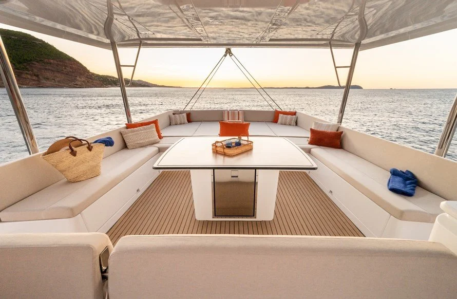 Une zone de détente sur un bateau avec vue sur la mer au coucher du soleil, comprenant un canapé en forme de U avec des coussins et une table centrale.