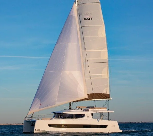 A white sailing catamaran with large sails on blue water, under a clear sky.