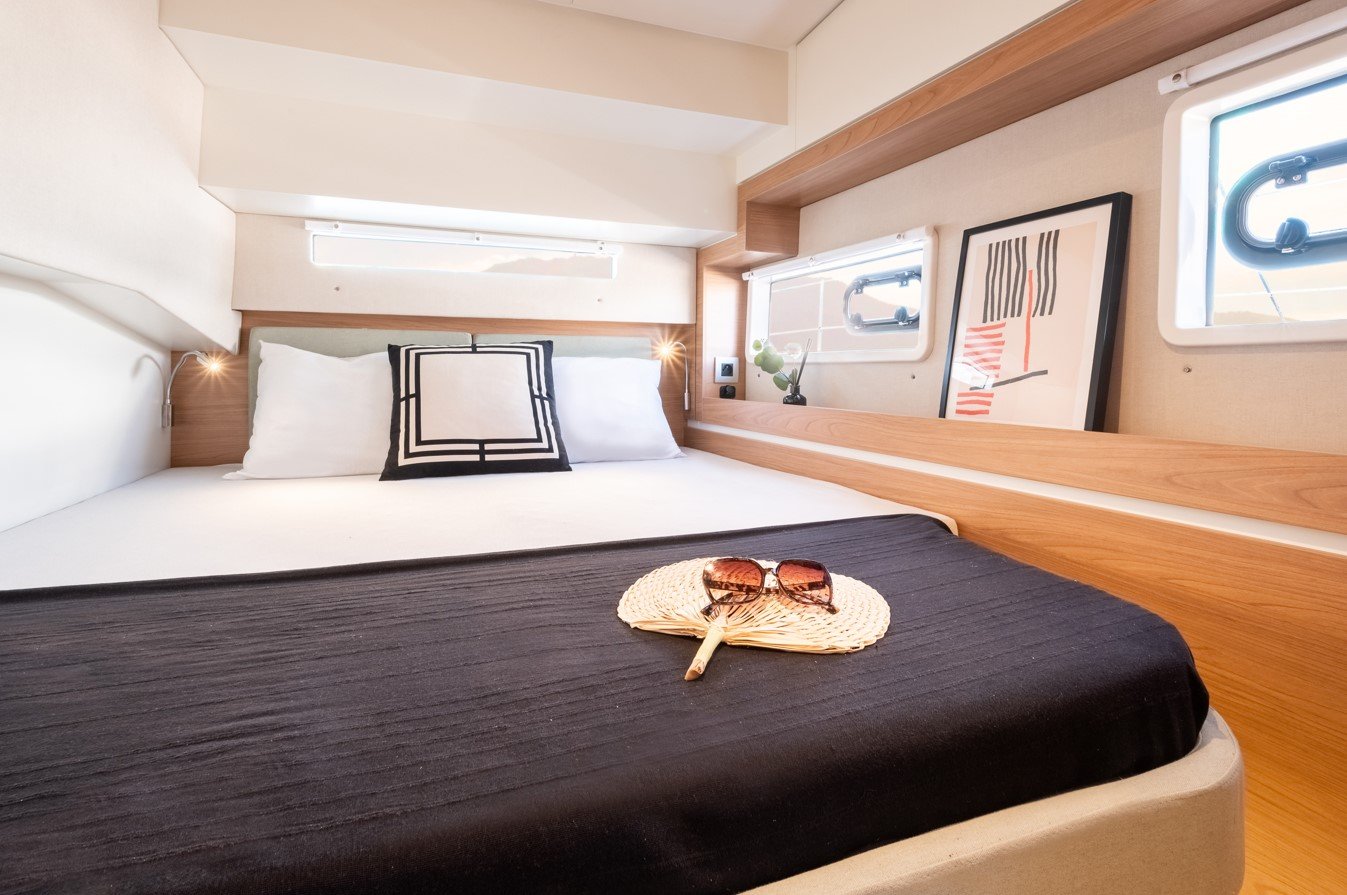 Lit double avec coussins et lunettes de soleil sur un ventilateur en osier dans une cabine de bateau moderne, avec fenêtres et décoration minimaliste.