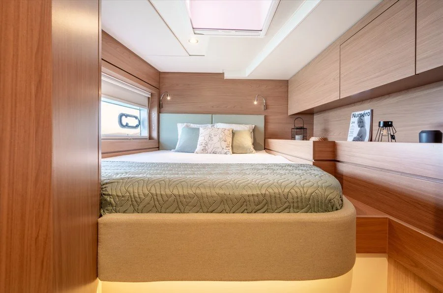 Chambre moderne avec lit double, coussins, fenêtre, et luminaires muraux en bois clair.