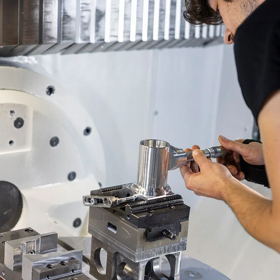 Ein Mensch arbeitet an einer CNC-Fräsmaschine, die ein metallisches Bauteil verarbeitet.