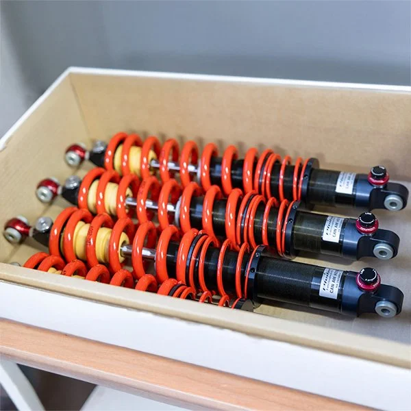 Verschiedene Stoßdämpfer in einer Holzschachtel, einige mit roten, einige mit schwarzen Schutzkappen.
