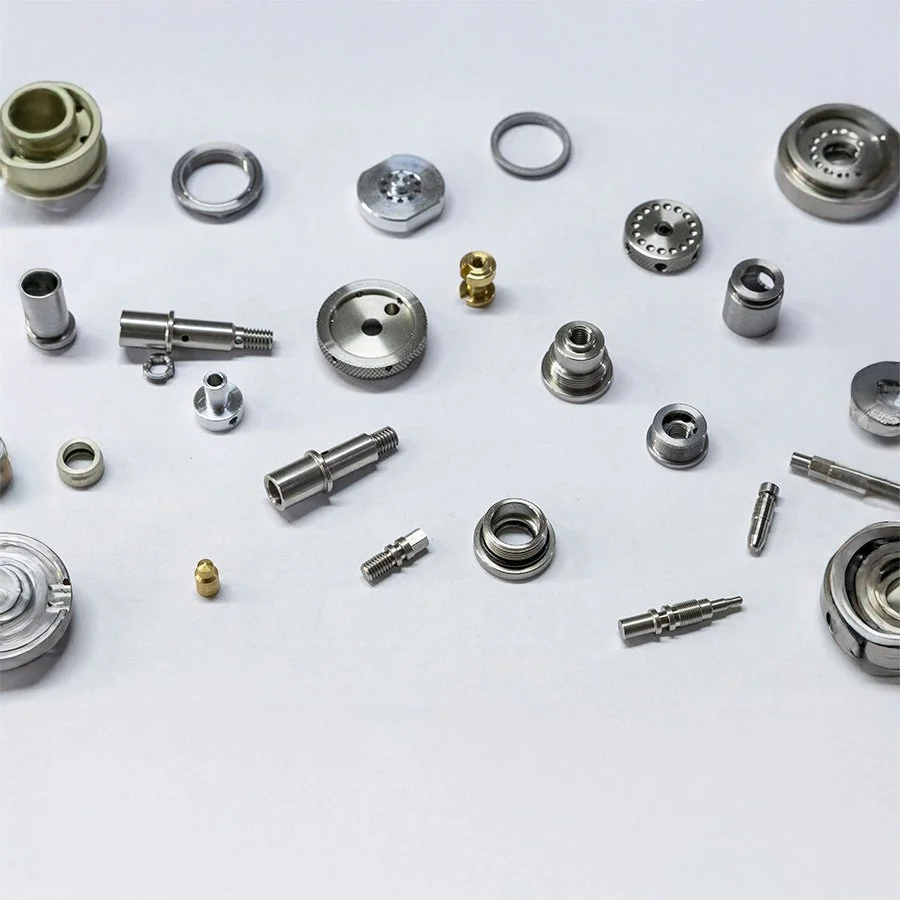 Verschiedene kleine Metallteile und Komponenten, die wahrscheinlich Teile eines technischen oder mechanischen Geräts sind, auf einer weißen Oberfläche