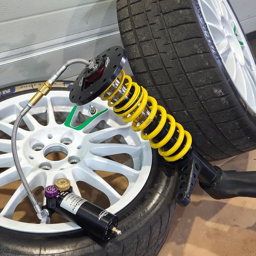 Fahrwerk mit gelbem Federungssystem und Autoreifen auf weißem Felgen auf einer Werkbank.