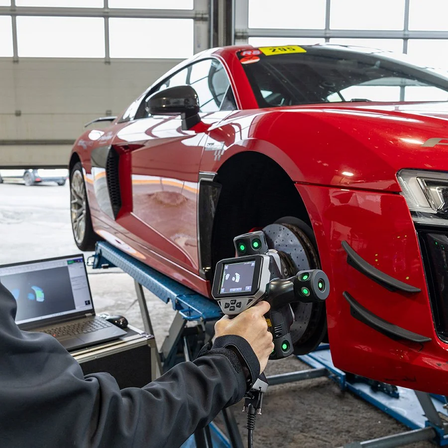 Messgerät wird an einem roten Rennwagen im Prüfstand befestigt, um aerodynamische Tests durchzuführen, mit Laptop im Hintergrund im Parkhaus.