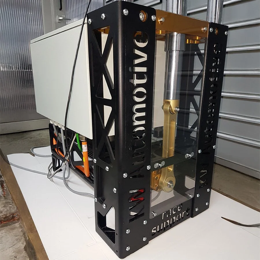 Ein technisches Gerät mit schwarzem Rahmen, mehreren Kabeln, einer weißen Box und metallischen Komponenten, das vermutlich eine Maschine oder ein technisches System ist.