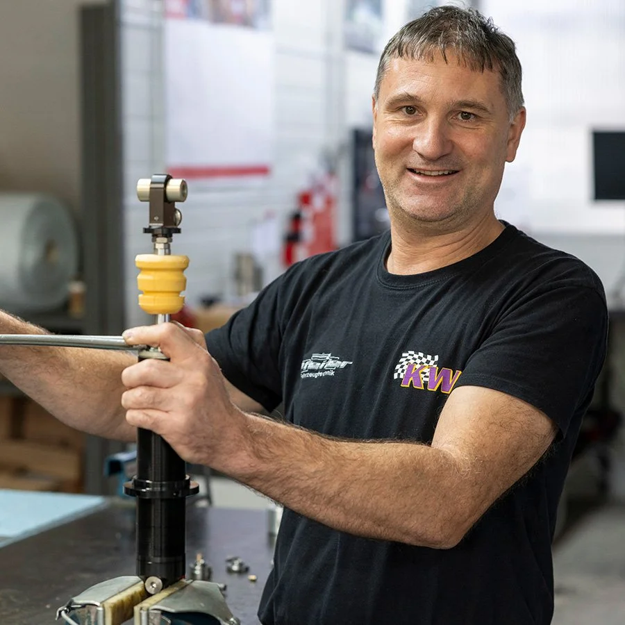 Ein lachender Mann bei der Arbeit in einer Werkstatt, der ein Rad an einem speziellen Gerät befestigt.