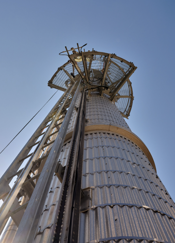 Low-angle view of a tall metal communication or observation tower with platforms and ladders, set against a clear blue sky.