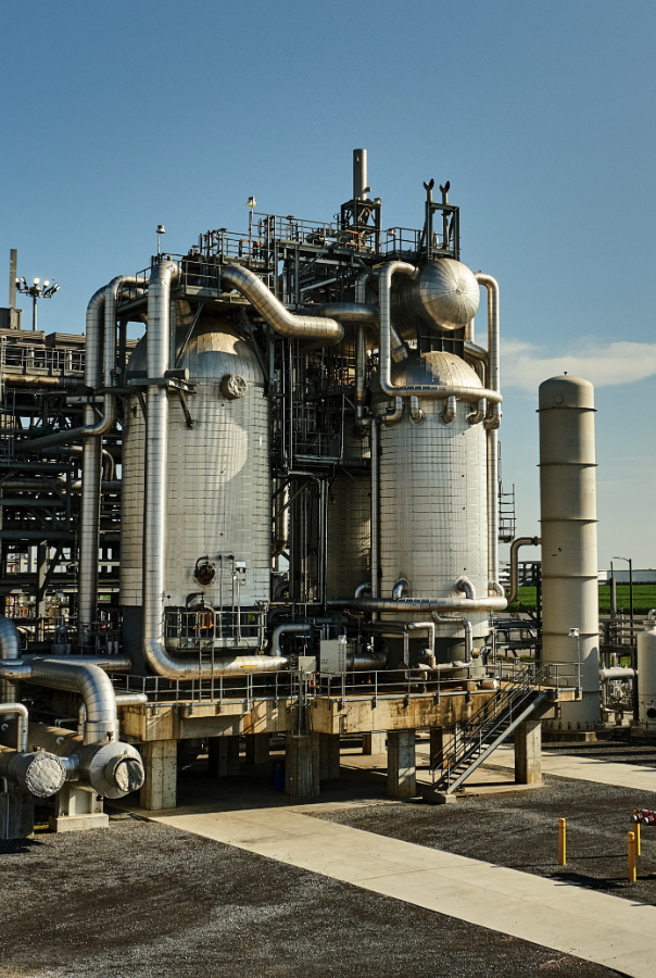 Industrial facility with large metal tanks, pipes, and structural supports under a clear blue sky.