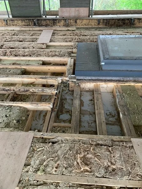 Unfinished flooring with exposed wooden floor joists and concrete, with some flooring materials nearby.