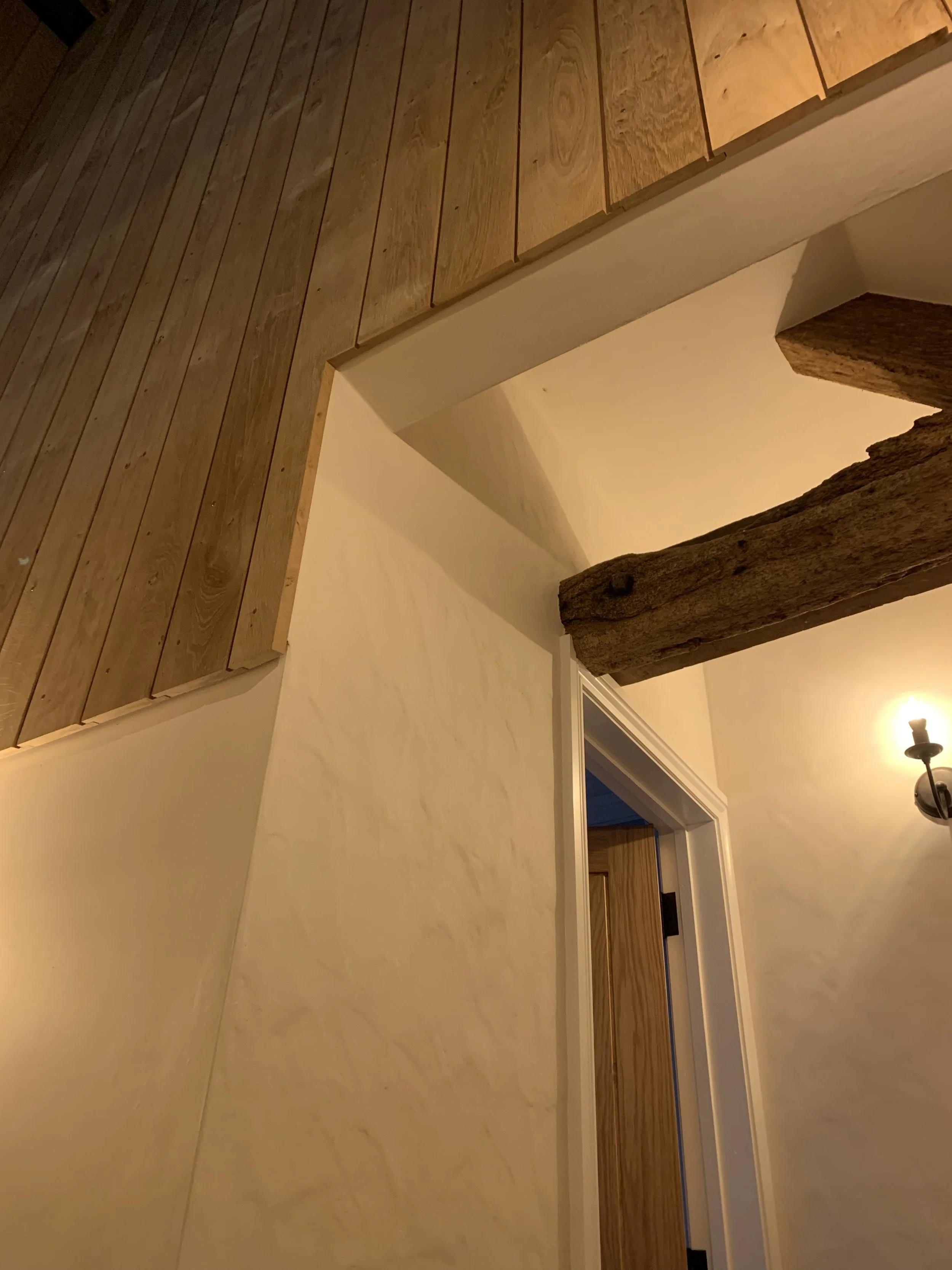 Interior view of a ceiling and wall with wooden beams, wood-paneled ceiling, and a door frame.