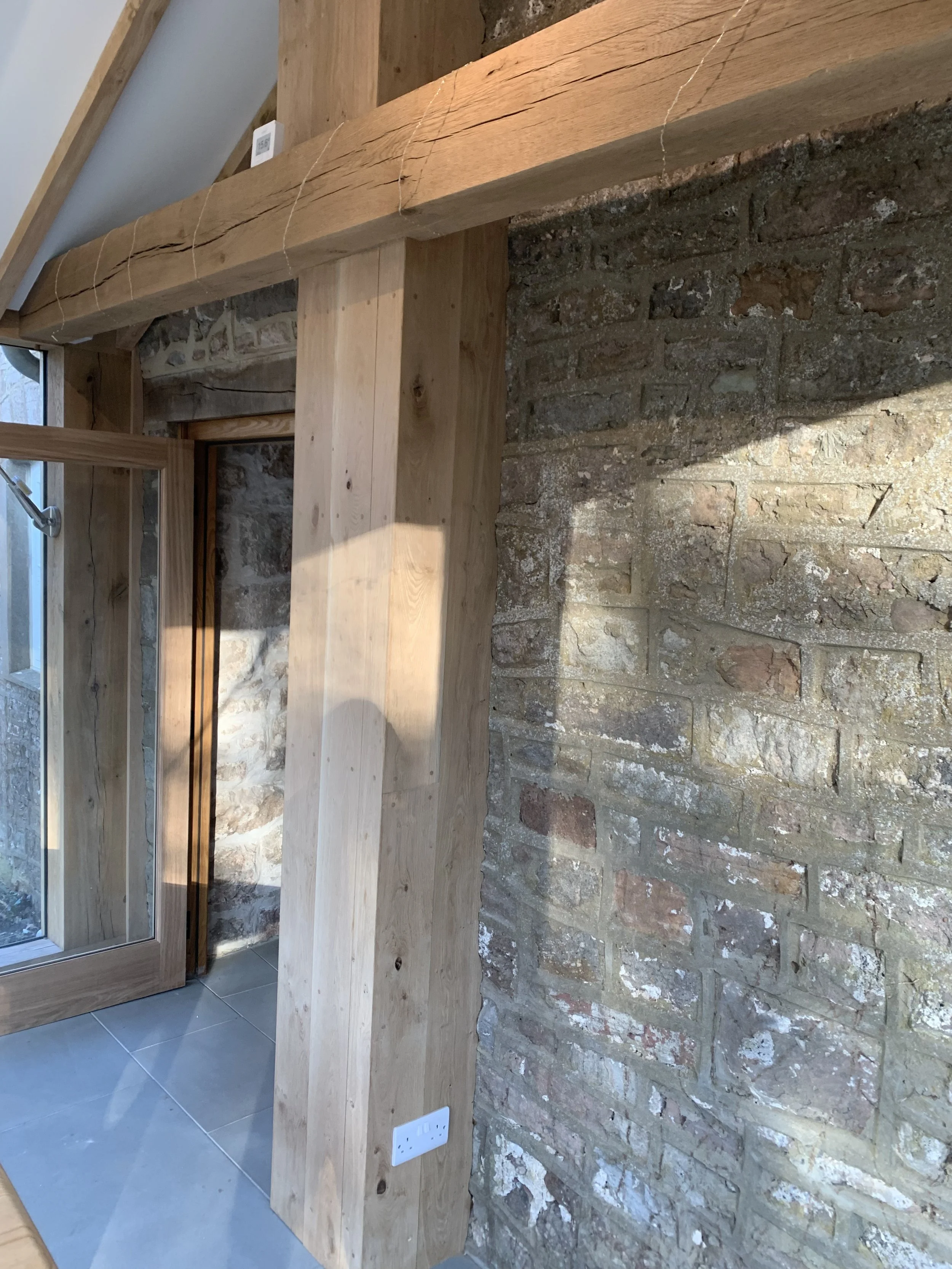 Interior corner of a room with exposed brick wall, wooden beams, and a partially open glass door with wooden trim.