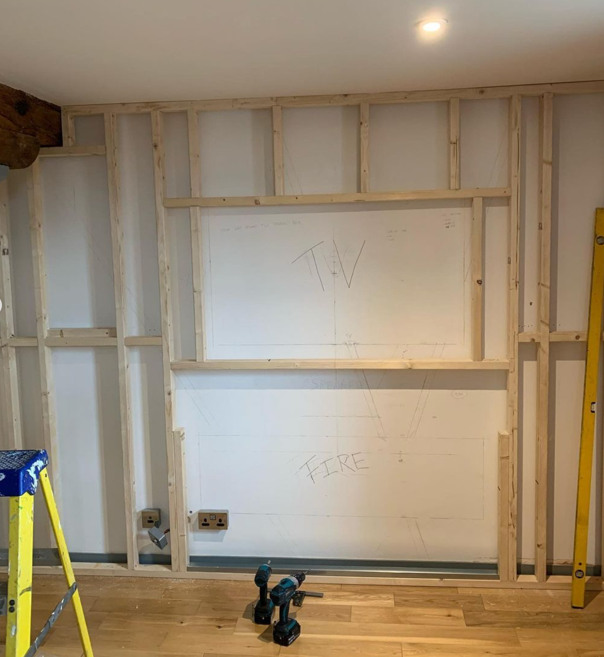 Interior wall framing with a whiteboard and construction tools, including a ladder and power drills, in a room under renovation.